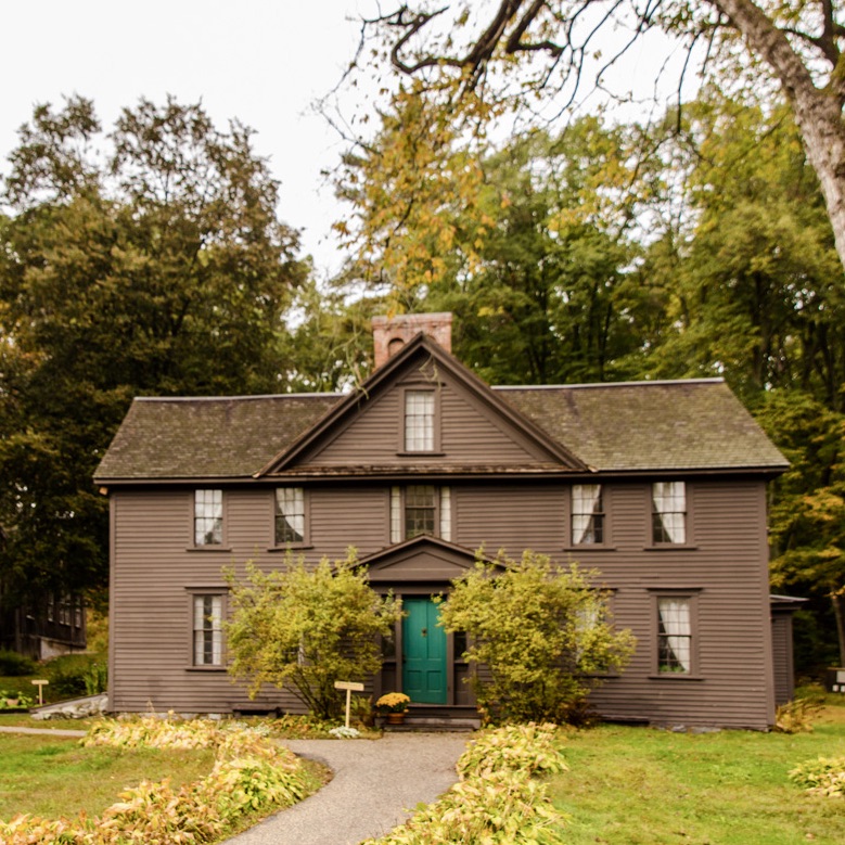 A two-story brown house surrounded by trees in autumn.